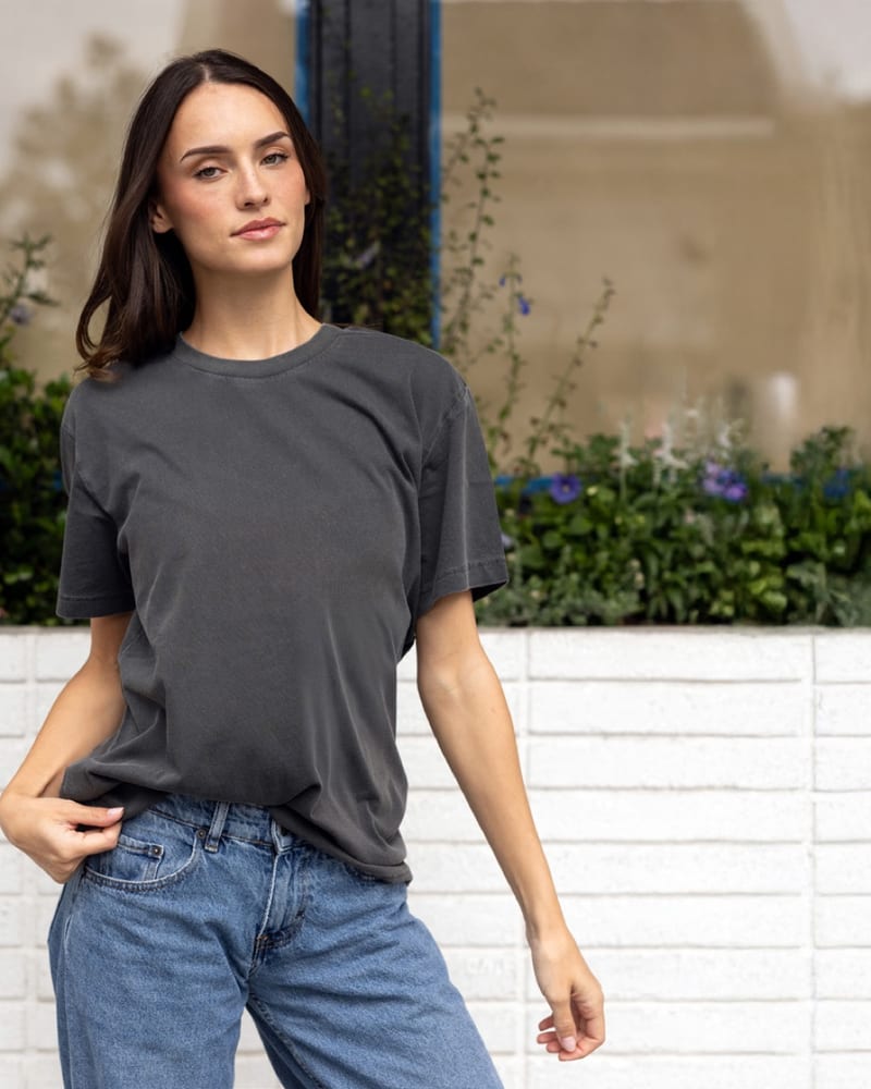 A woman in the PRM180PT tee in pigment black, standing by a white brick planter