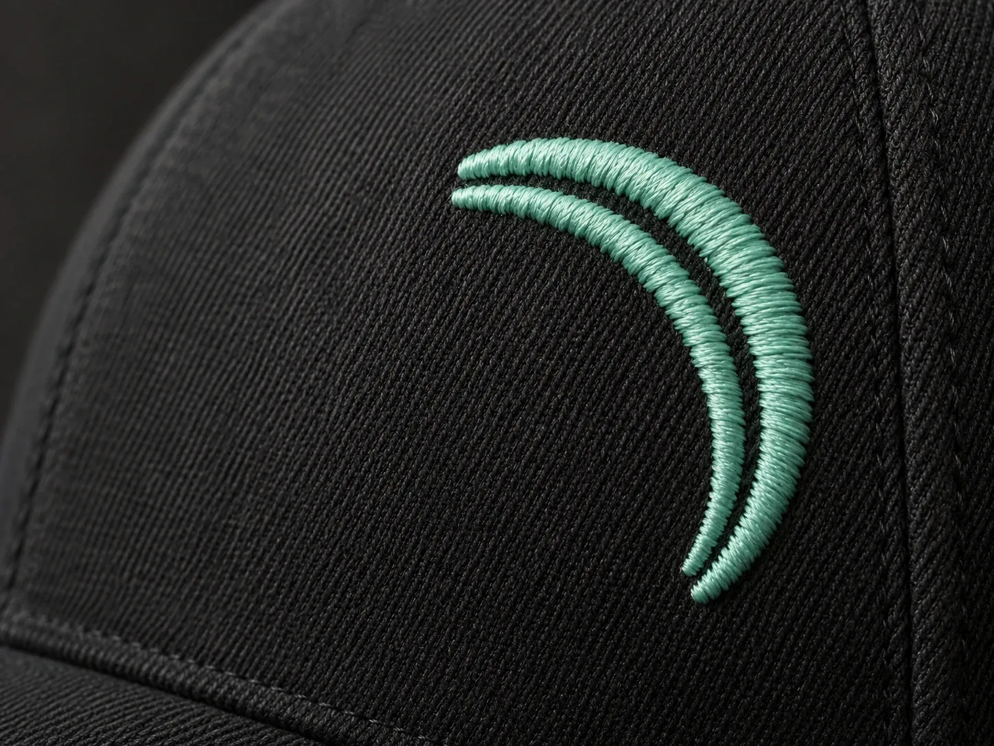 Close detail of mint embroidered crescent marks on black cap twill