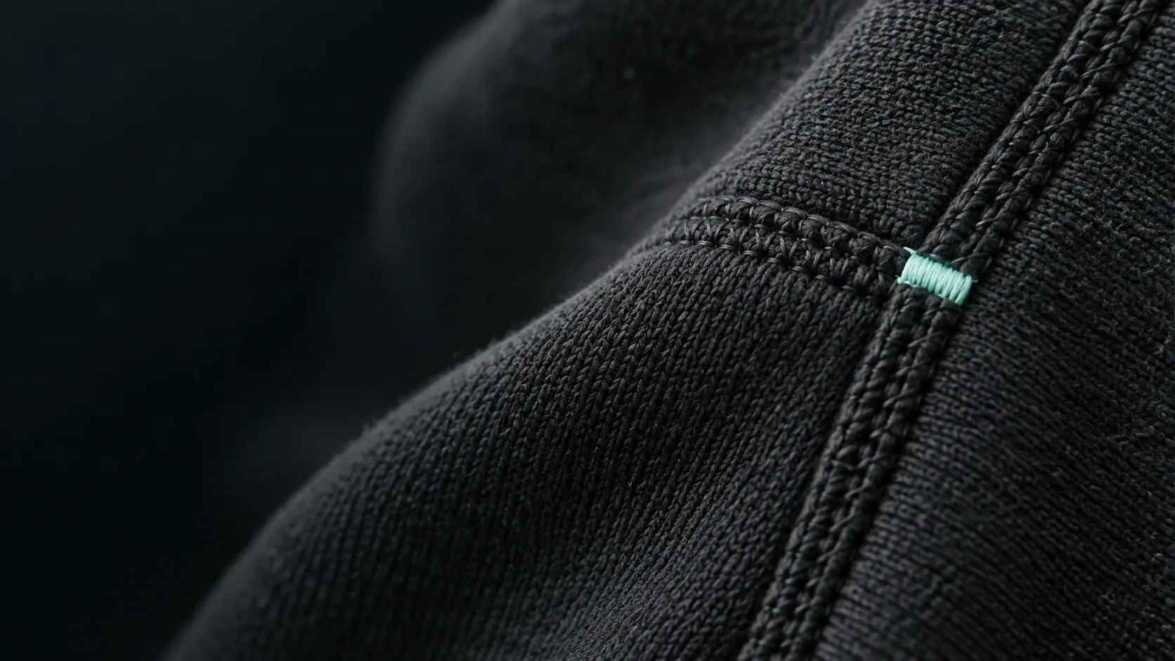 Close detail of black heavyweight fleece with a double-stitched seam and a small mint thread tab