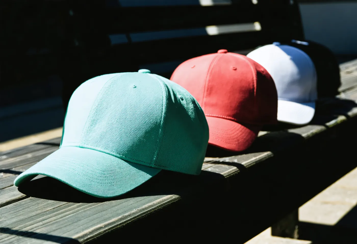 A row of unbranded six-panel caps on a dark bench, one turned to show the crown seam