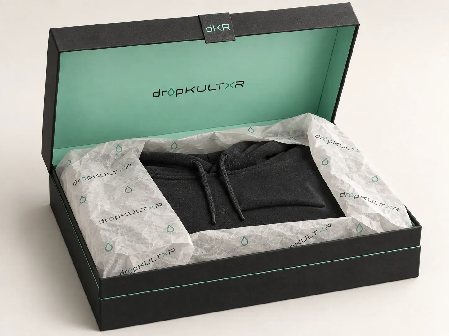 Concept packaging: the black box open on a mint interior, a plain charcoal hoodie folded in branded tissue