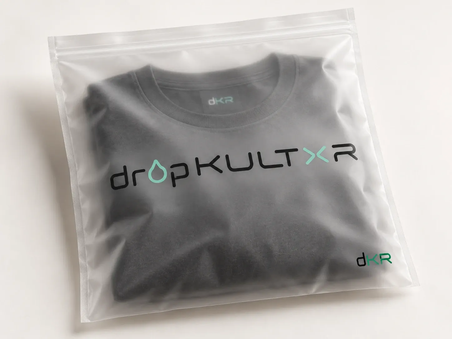 Concept packaging: a folded charcoal tee in a frosted garment bag printed with the dropKULTXR wordmark