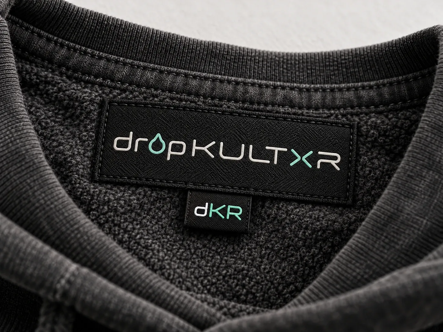 Concept detail: a woven black neck label reading dropKULTXR with a dKR mark, inside a charcoal fleece collar