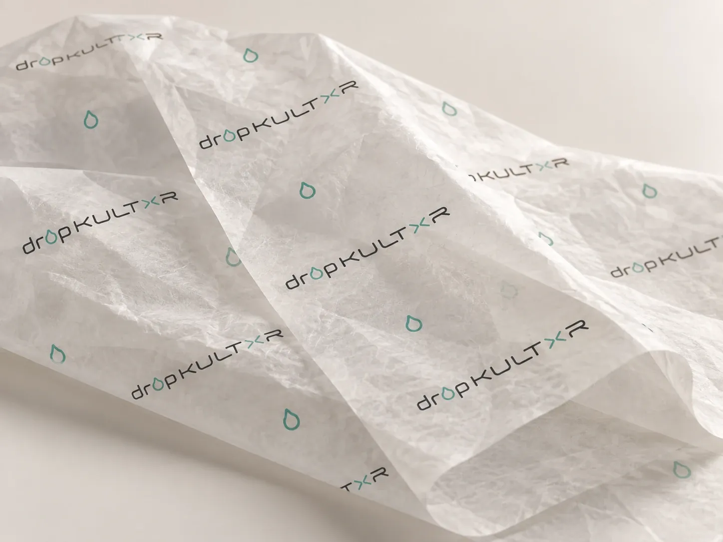 Concept packaging: bone tissue paper printed with spaced dropKULTXR wordmarks and mint teardrops